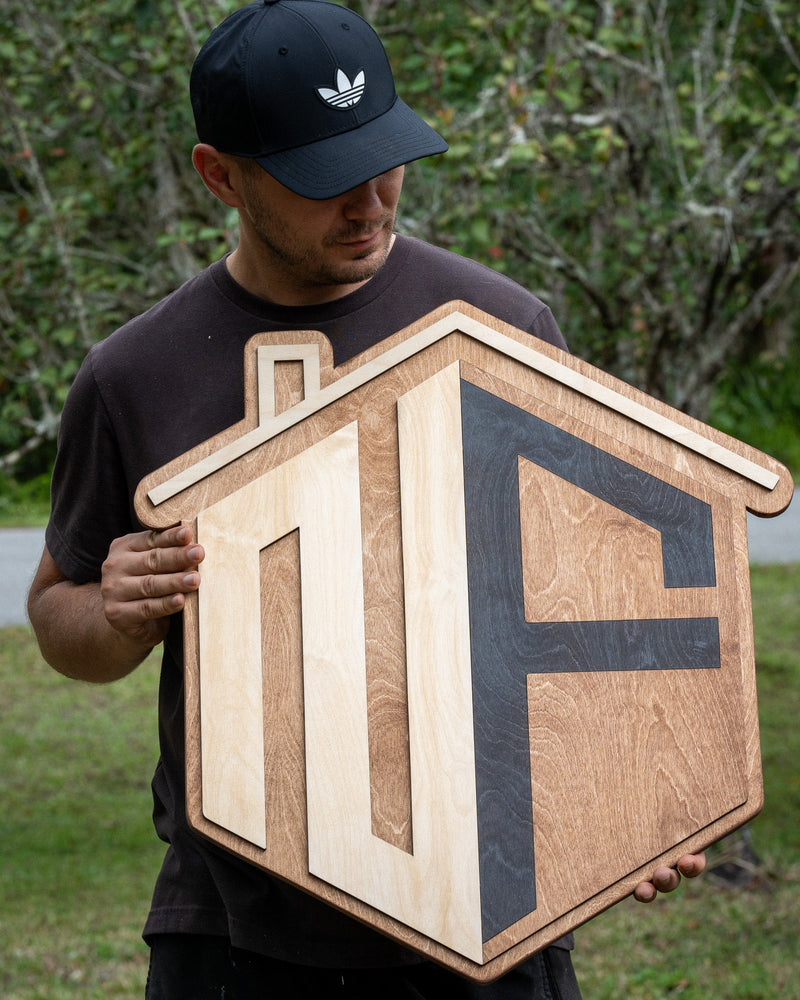 Andrey from WoodHarmonyUS holding a large 36-inch diagonal personalized house-shaped logo sign. Custom 3D business signage made of Baltic Birch in Tampa.