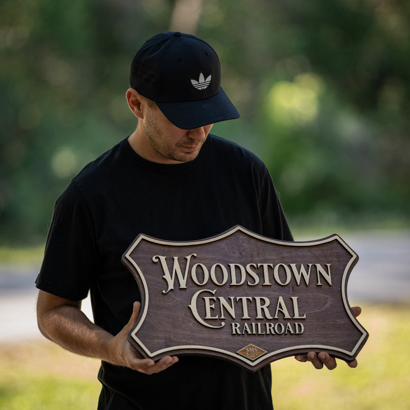 Andrey from WoodHarmonyUS holding a custom vintage-style Woodstown Central Railroad 3D wood sign with ornate shield shape and dark walnut finish
