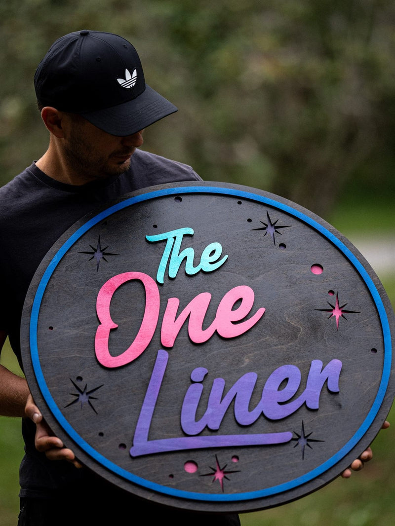 Custom round wooden The One Liner sign made from layered Baltic Birch plywood with colorful raised lettering and star details.