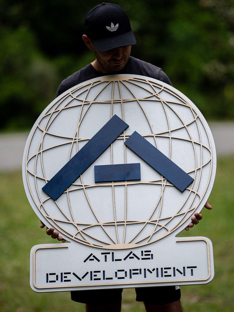 Layered wood lobby sign for Atlas Development: an open birch globe cut as fine latitude and longitude ribs, crossed by two navy bars above the company name.