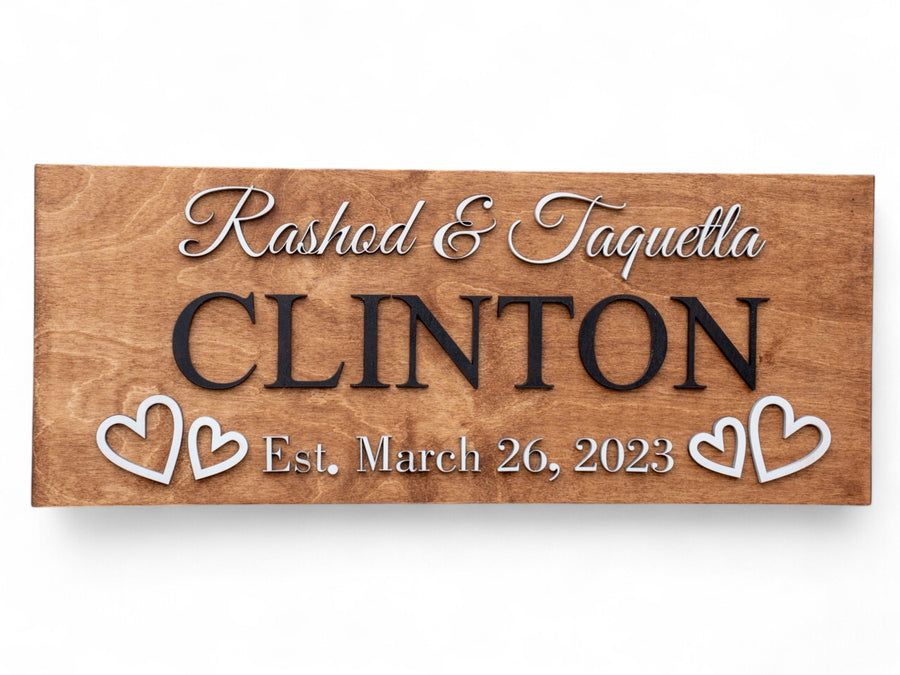 Walnut wood sign with raised lettering reading Rashad & Taquella, CLINTON, Est. March 26, 2023, flanked by two white hearts.