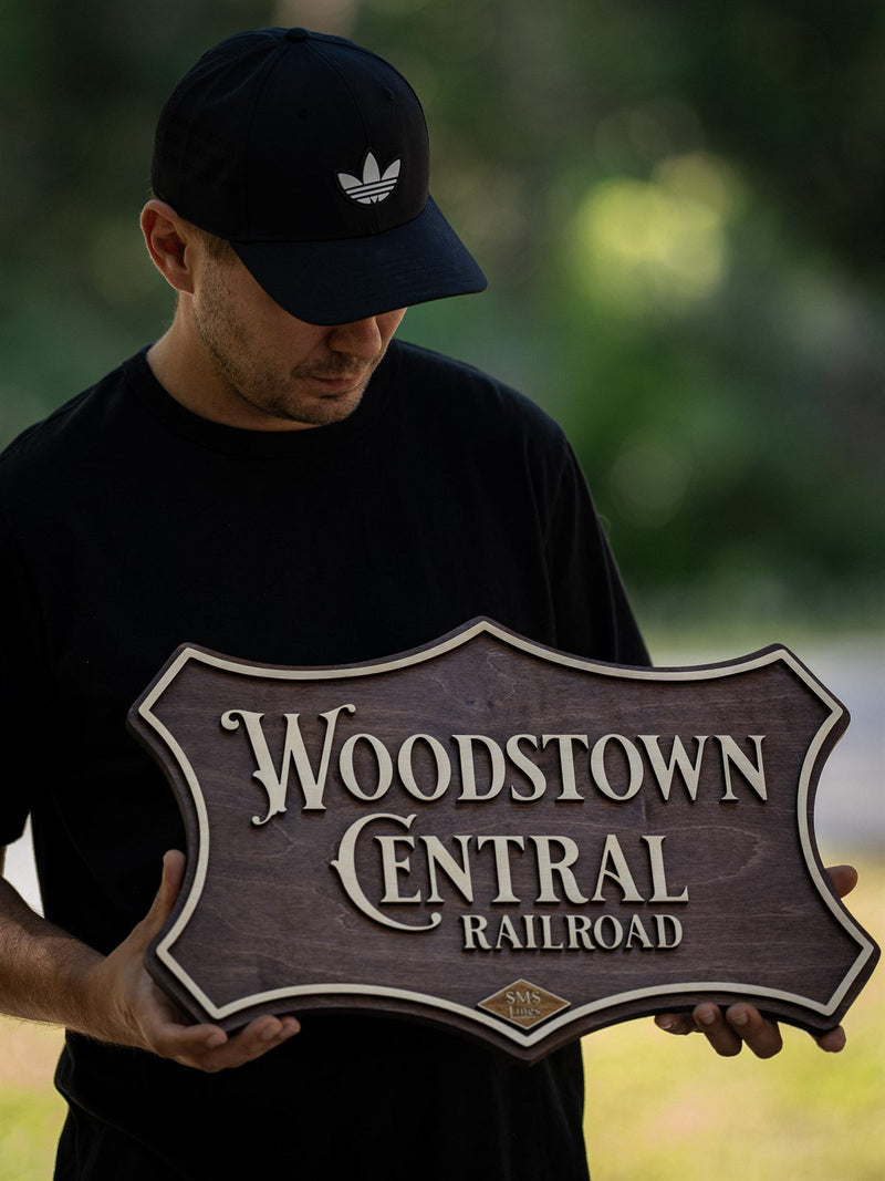 Dark walnut scrolled cartouche wood sign with cream serif lettering reading Woodstown Central Railroad
