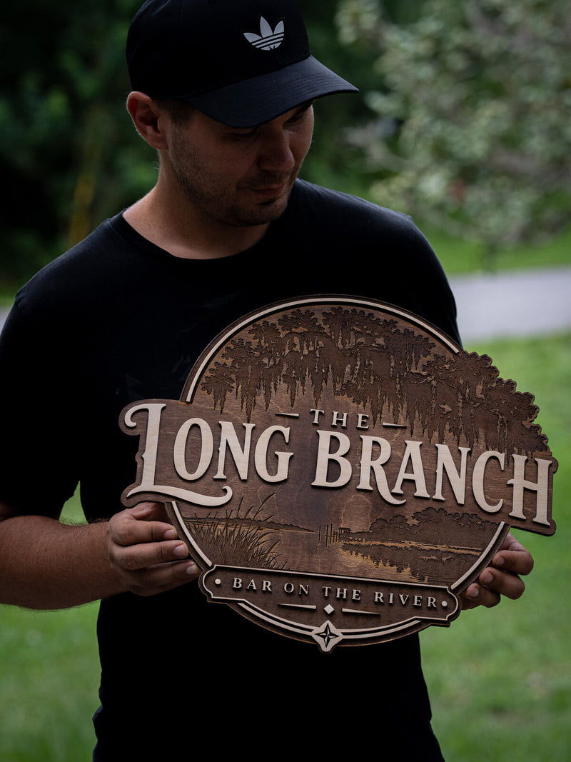 Round dark walnut bar sign deeply engraved with a Spanish moss oak canopy and a river scene, reading The Long Branch, Bar on the River