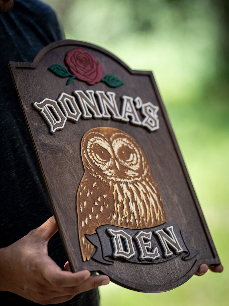 Tall arched dark walnut plaque with a deep red rose and a large engraved tawny owl, reading Donna's Den in cream blackletter