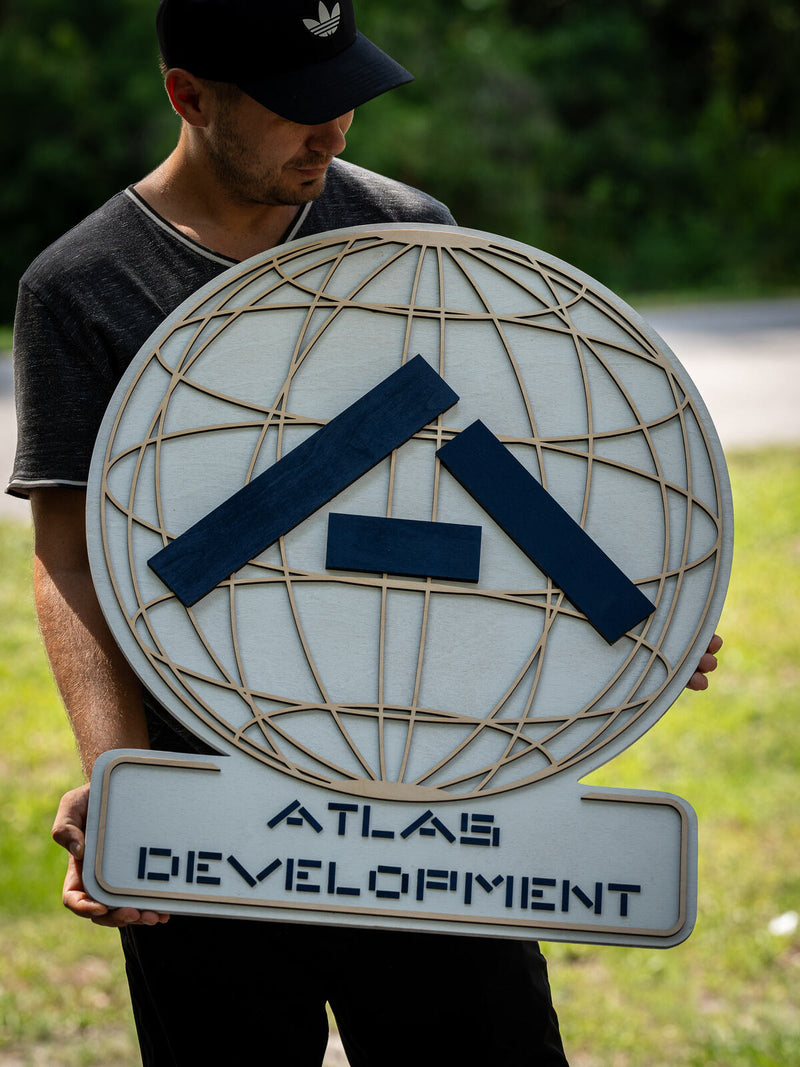 Pale birch fretwork globe of thin engraved latitude lines with a navy chevron, mounted over a cut-out plate reading Atlas Development