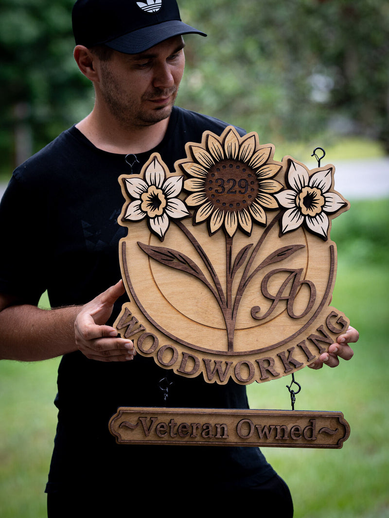 Two-piece hanging wood sign with three layered flowers above a circle carrying a script AO monogram, with a Veteran Owned rider board below