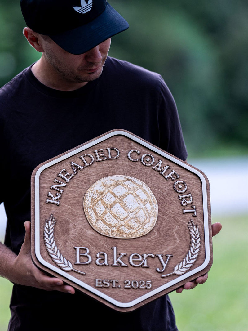 Hexagonal reddish-brown wood bakery sign for Kneaded Comfort with an engraved sourdough boule and cream wheat sheaves