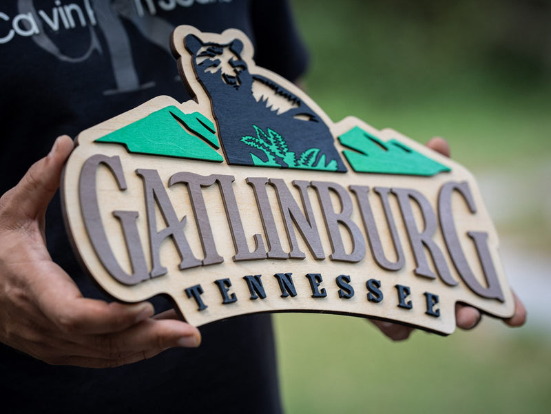 Wide layered wood destination sign reading Gatlinburg Tennessee with a black bear among teal hills and grey mountains