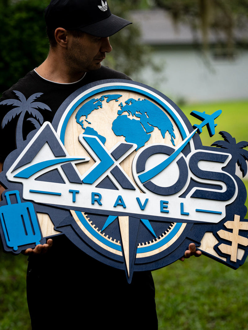 Wide navy, blue and birch layered wood lobby sign for AXOS Travel with a globe, angular wordmark, compass rose, rolling suitcase and palm trees