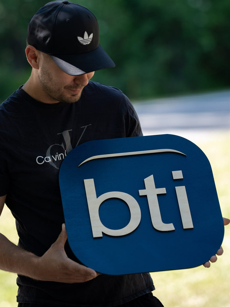 Rounded-square two-tone blue wood logo tile with large white cut-out lowercase letters reading bti