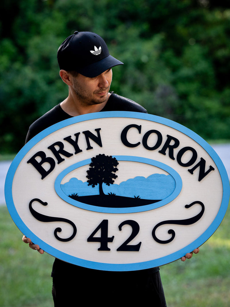Large horizontal oval house sign with a sky blue outer band on cream, black serif lettering reading Bryn Coron and a large number 42