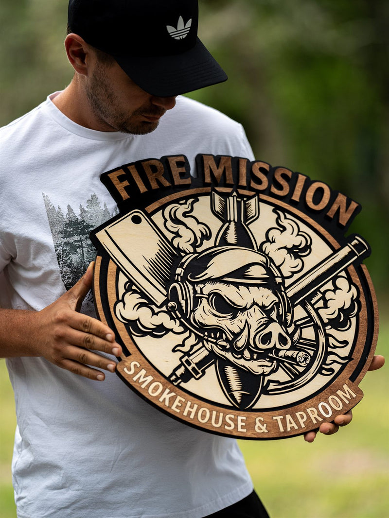 Round wood restaurant sign for Fire Mission Smokehouse and Taproom with an engraved helmeted skull, cleaver and rolling pin