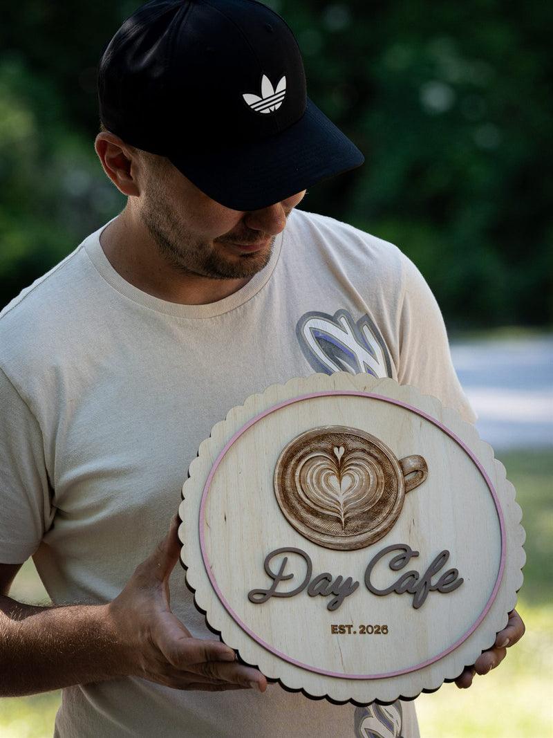 Round pale birch cafe sign with a scalloped edge and an engraved latte cup with heart and fern latte art, reading Day Cafe