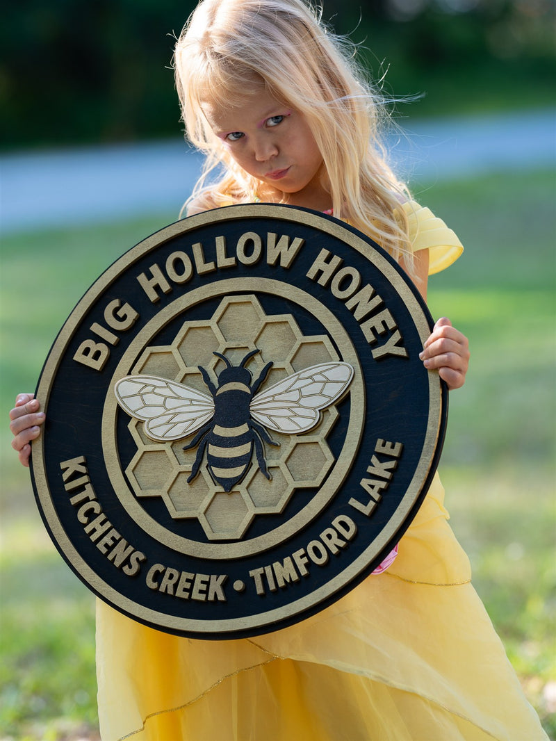 Round navy and gold wood sign for Big Hollow Honey with a layered bee on a honeycomb and arched lettering