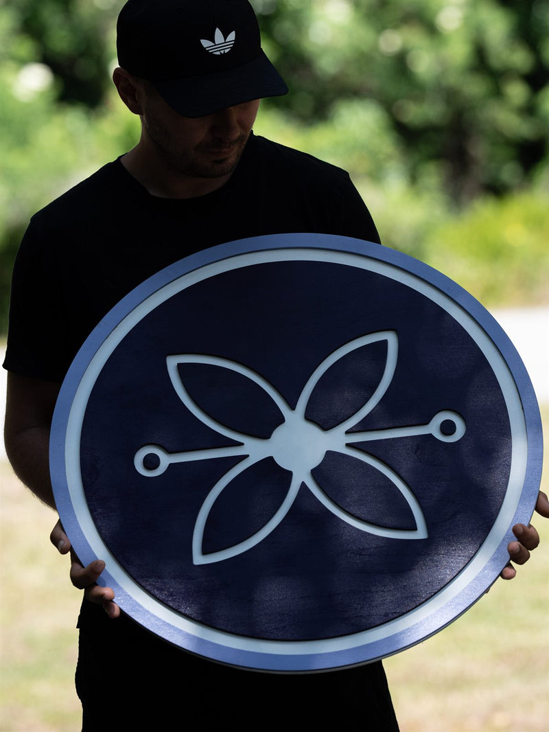 Round deep navy wood sign with a pale powder blue outer ring and an outlined four-petal flower or propeller mark