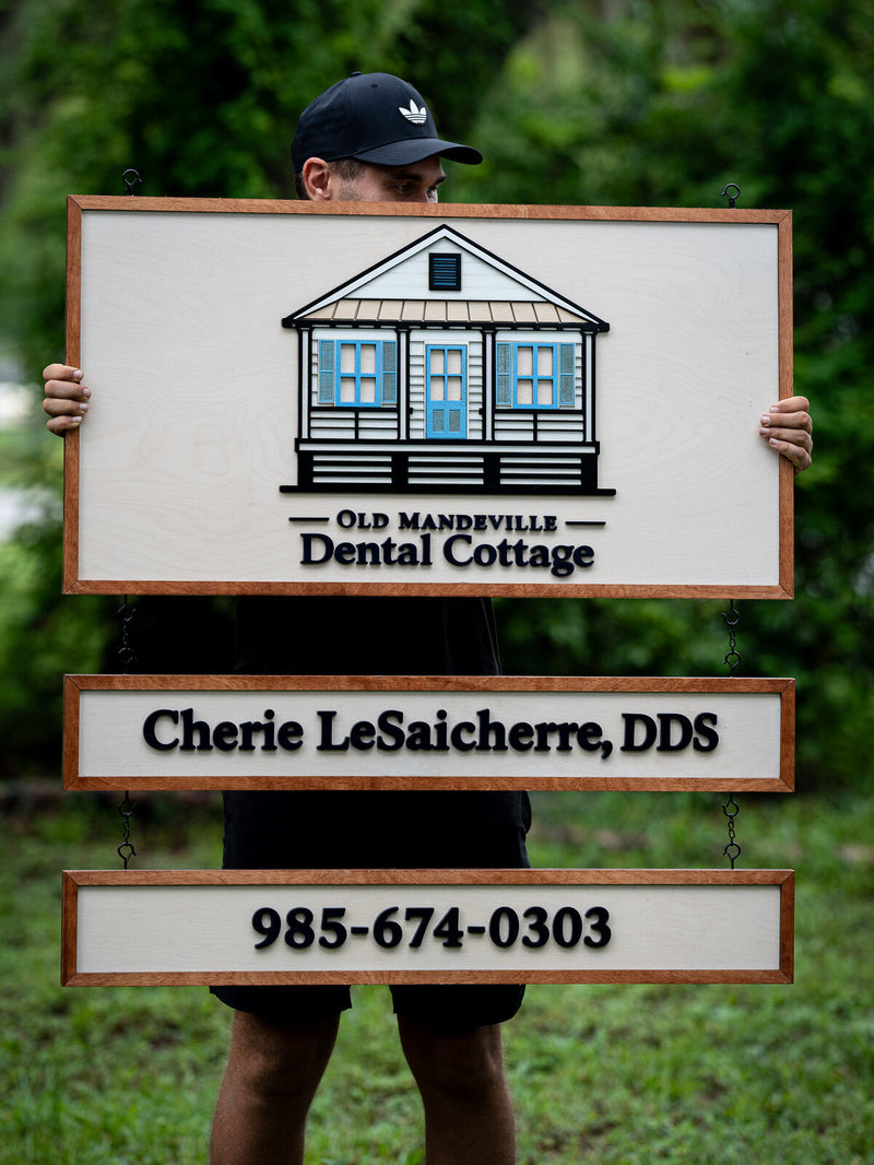 Three-tier hanging wood dental sign with a cream panel showing a layered Creole cottage, and two smaller chained boards below