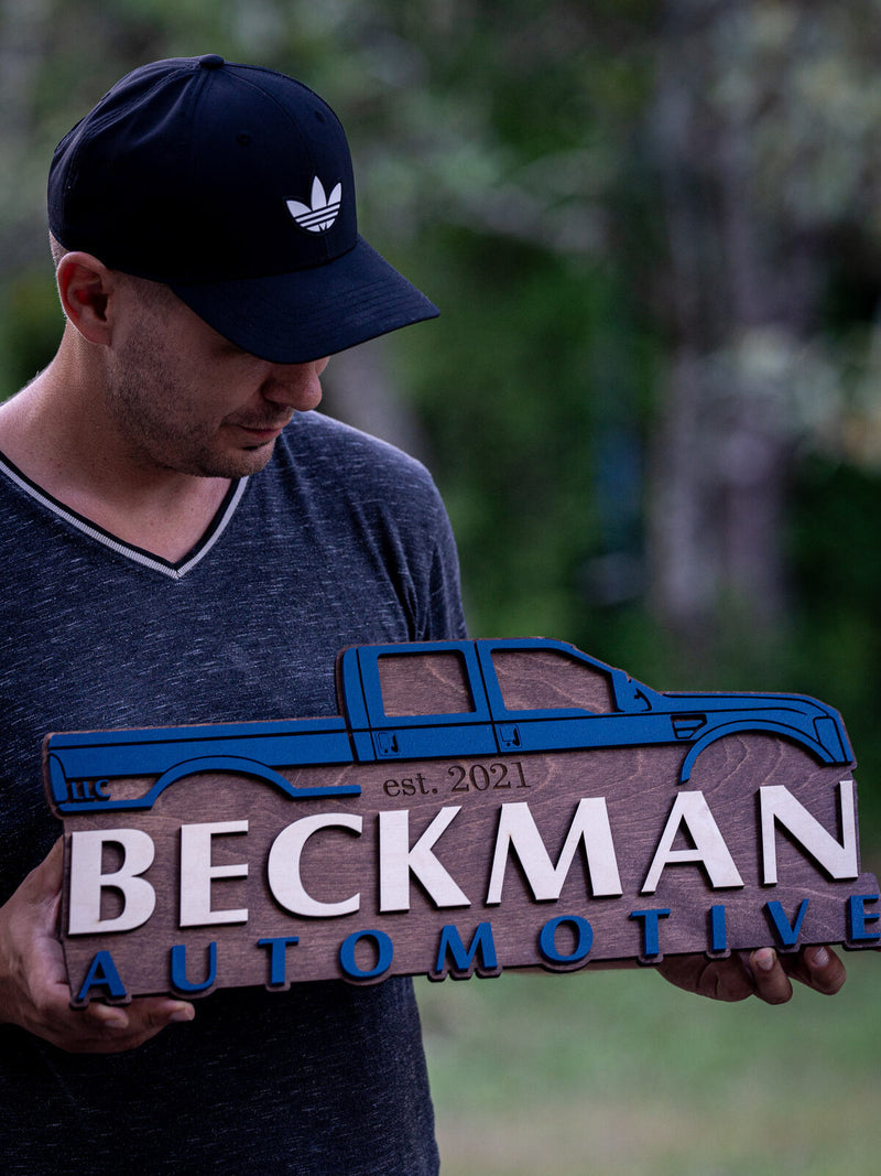 Long horizontal brown wood auto shop sign with a blue cut-out crew cab pickup silhouette above cream and blue lettering reading Beckman Automotive