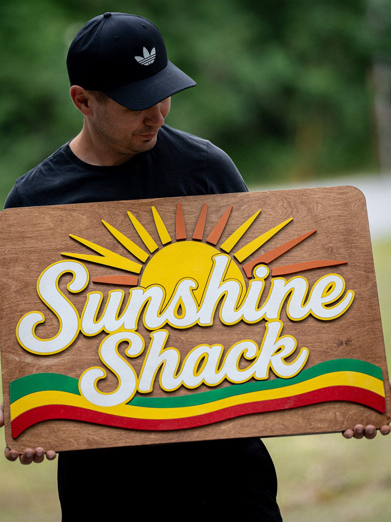 Rectangular mid-brown wood beach bar sign with a layered orange and yellow rising sun and green, yellow and red stripes