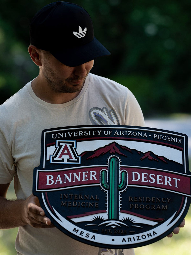 Shield-shaped wood crest for the University of Arizona Phoenix Banner Desert internal medicine residency with a saguaro cactus and red mountains