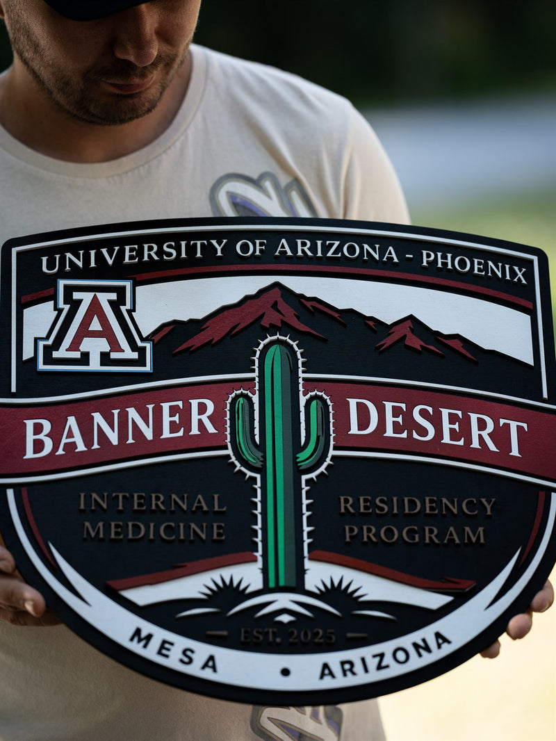 Close framing of the Banner Desert residency wood crest showing the layered cactus, mountains and established 2025 line