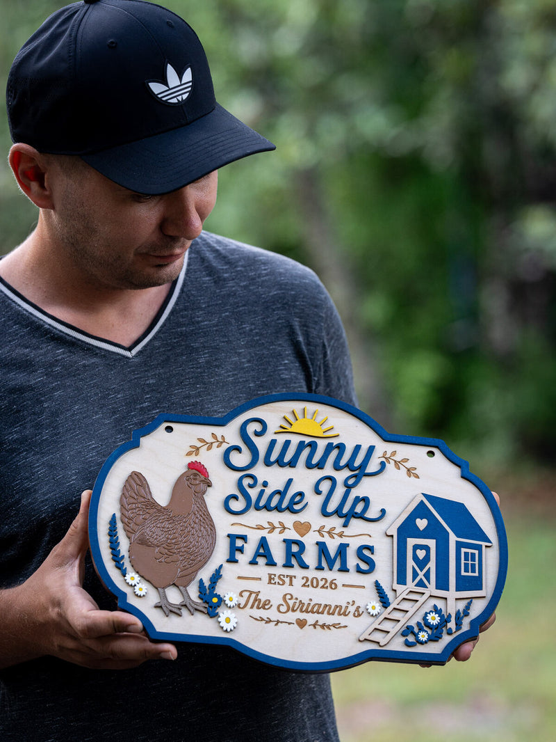 Cloud-lobed pale birch farm sign with a royal blue edge showing a brown hen, a blue chicken coop and a rising sun, reading Sunny Side Up Farms