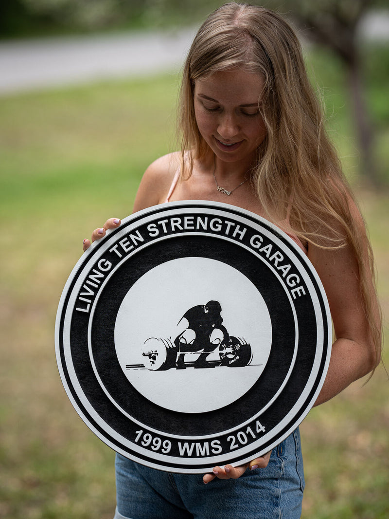 Large concentric black and white wood gym sign with a silhouette of a lifter mid-deadlift on a white inner circle