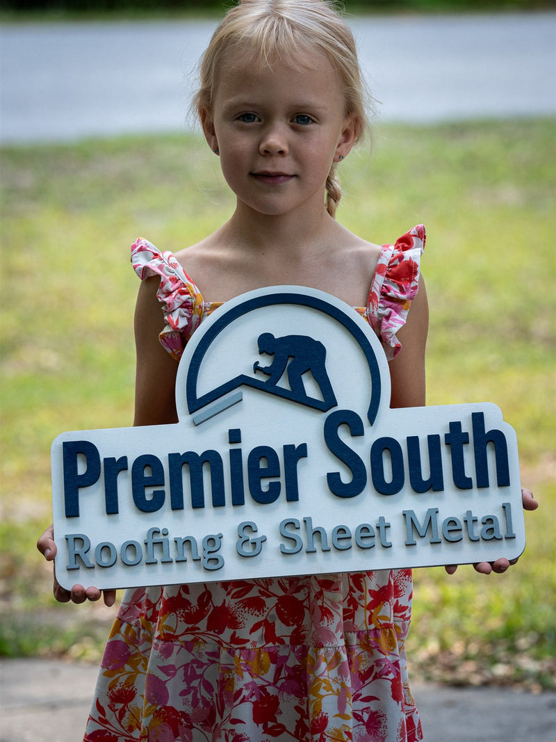 Shield-shaped wood logo sign for Premier South Roofing and Sheet Metal with a blue roofer emblem on a pale blue base