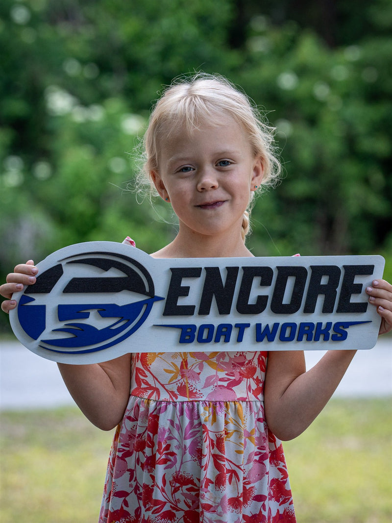 Layered wood business logo sign for Encore Boat Works, navy and royal blue wave monogram over block lettering, held outdoors
