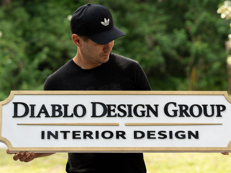 Wide cream wood nameplate lobby sign with a dark keyline border reading Diablo Design Group, Interior Design