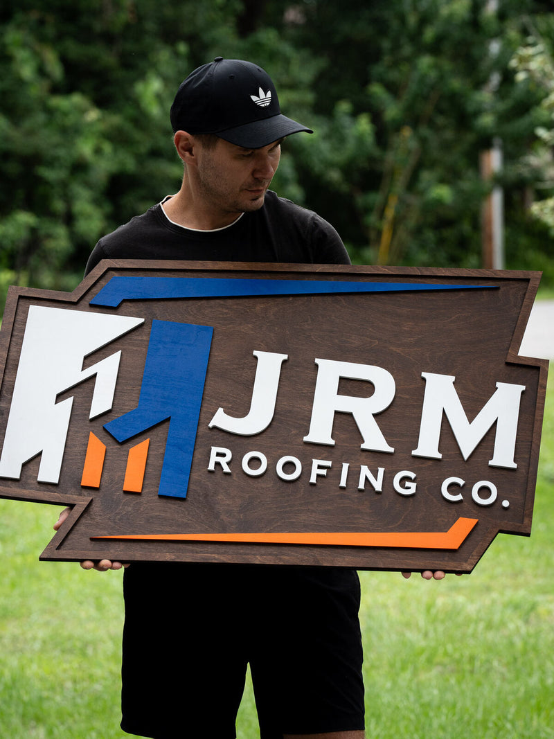 Angular chevron-shaped walnut contractor sign with a white, blue and orange geometric rooftop mark reading JRM Roofing Co