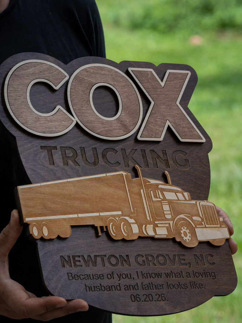 Large shaped wood sign with cream-outlined walnut lettering reading Cox Trucking and a tan cut-out semi truck across the middle